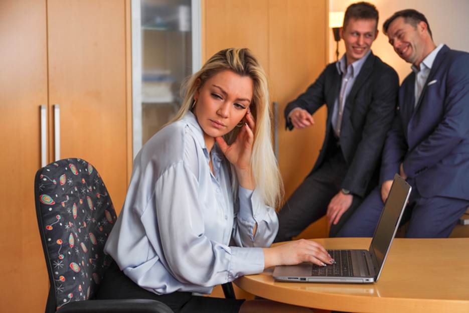Woman looking stressed while male coworkers laugh at her - Sexual Discrimination